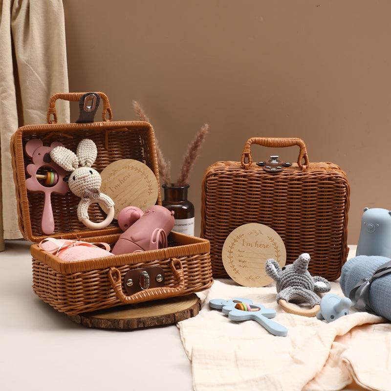 Das Ayla Baby Geschenk zur Geburt von Hello World zeigt zwei offene Weidenkörbe mit Babyspielzeug - gestrickter Hase, Koala-Greifling, Silikon-Schnuller, Holzrassel und Plüschtiere - auf einer Holzfläche neben einem geschlossenen Korb. Neutraler Hintergrund.