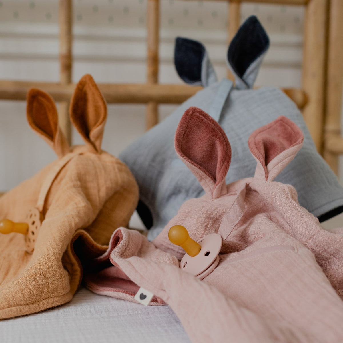 Diverse morbide coperte a canguro BIBS in diversi colori su un lettino nella stanza del bambino, una con un ciuccio.