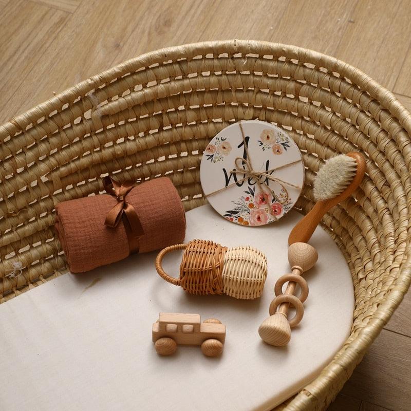 Das Carla Baby Geschenk zur Geburt von Hello World enthält einen braunen Wickel, einen Holzspielzeugbus, eine runde Meilensteinkarte, eine Babyhaarbürste, einen Holzrassel für die sensorische Entwicklung und ein Holzringspielzeug - hübsch arrangiert in einem gewebten Stubenwagen.