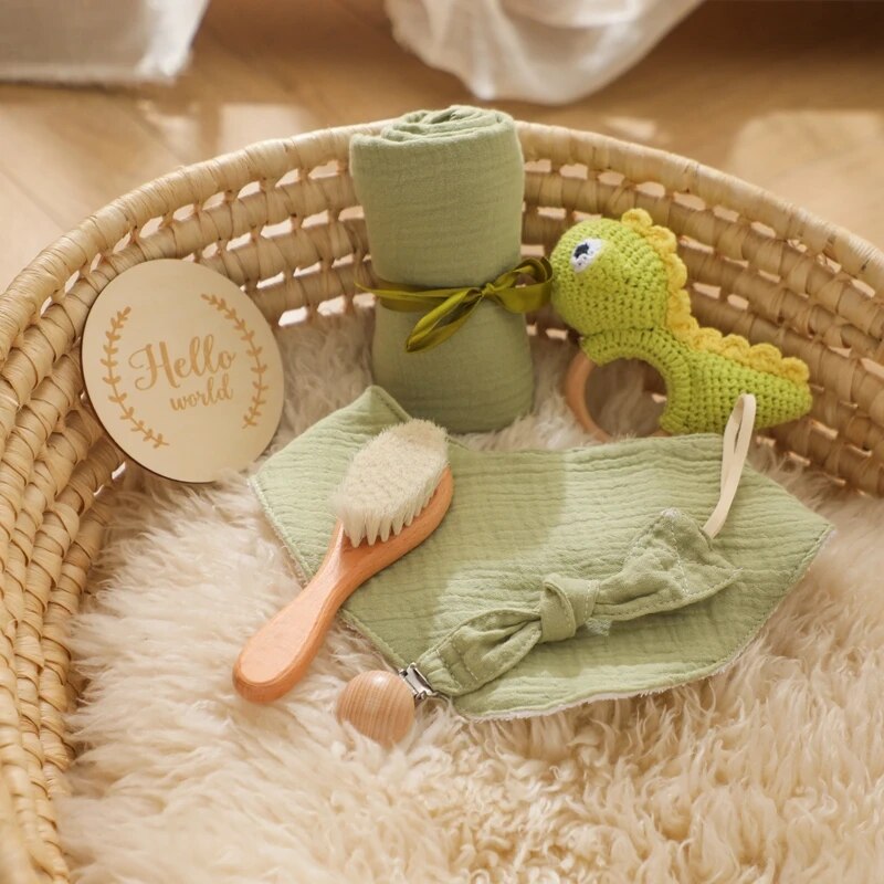 Das Alfredo Baby Geschenk zur Geburt von Hello World besteht aus einem geflochtenen Körbchen mit Fellfutter, grünem Musselintuch, gehäkelter Dinosaurier-Rassel, Schnullerkette, "Hello world"-Schild, Babybürste, grünem Schleifen-Stirnband und Schnuller.