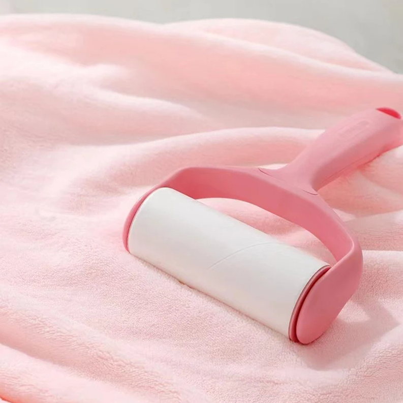 Auf dem weichen, hellrosa Hello World Badetuch mit Kapuze Hase (80x80cm) sitzt eine pinkfarbene Fusselrolle mit Griff, um Fusseln oder Tierhaare zu entfernen.