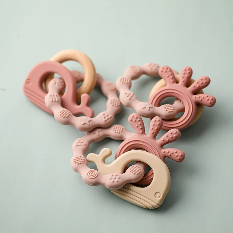 Der Hello World Beissring Walfisch Rosa (10,5 x 7 cm) zeigt ein pastellrosa Wal-Design mit einer strukturierten Oberfläche, die das Zahnen erleichtert, auf einem hellgrünen Hintergrund.