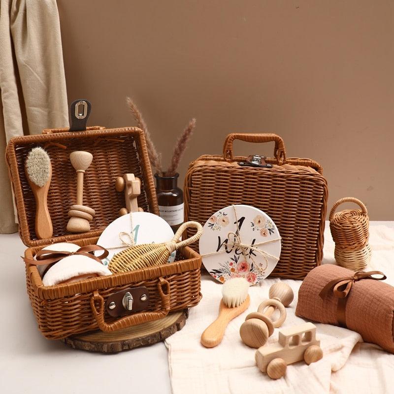 Das Hello World "Carla Baby Geschenk zur Geburt" Set besteht aus Weidenkörben und Holzspielzeug, darunter eine Holzrassel, ein Spielzeugauto, Bürsten und ein Blumenschild "1 Woche" - arrangiert auf beigem Stoff mit getrockneten Blumen.