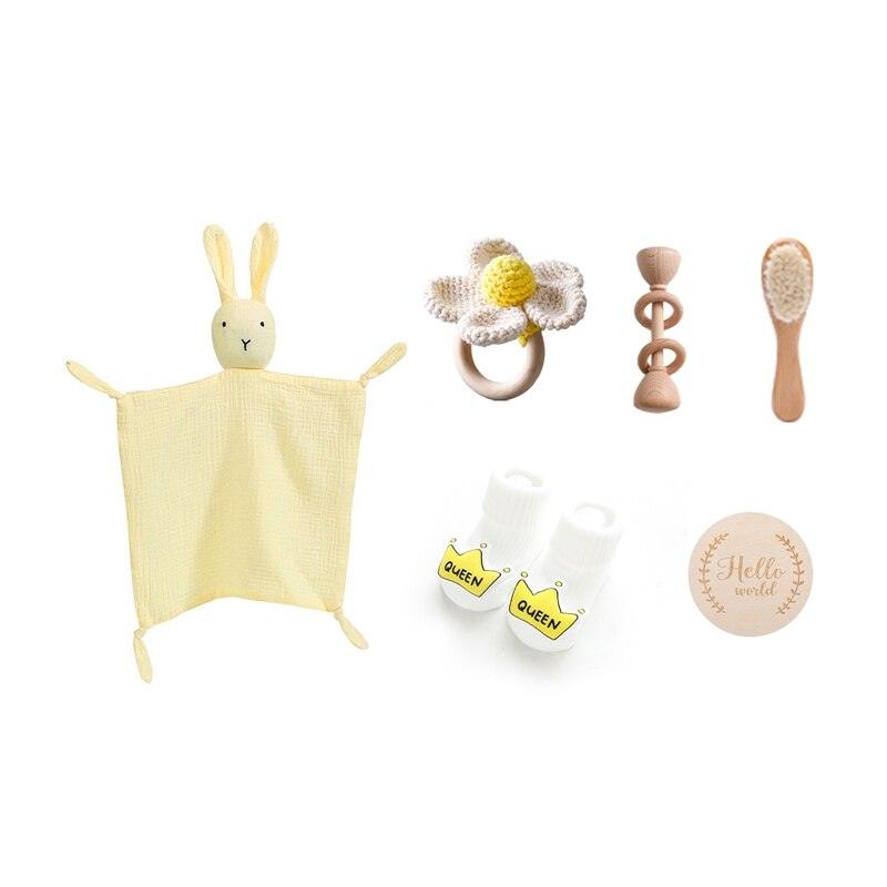 Das Fiona Baby Geschenk zur Geburt von Hello World besteht aus einer gelben Hasen-Schnuffeldecke, einem gehäkelten Rasselblume-Beißring, einer Holzrassel, einer Babybürste, weißen Queen-Socken und einer Hello World-Holzplakette.