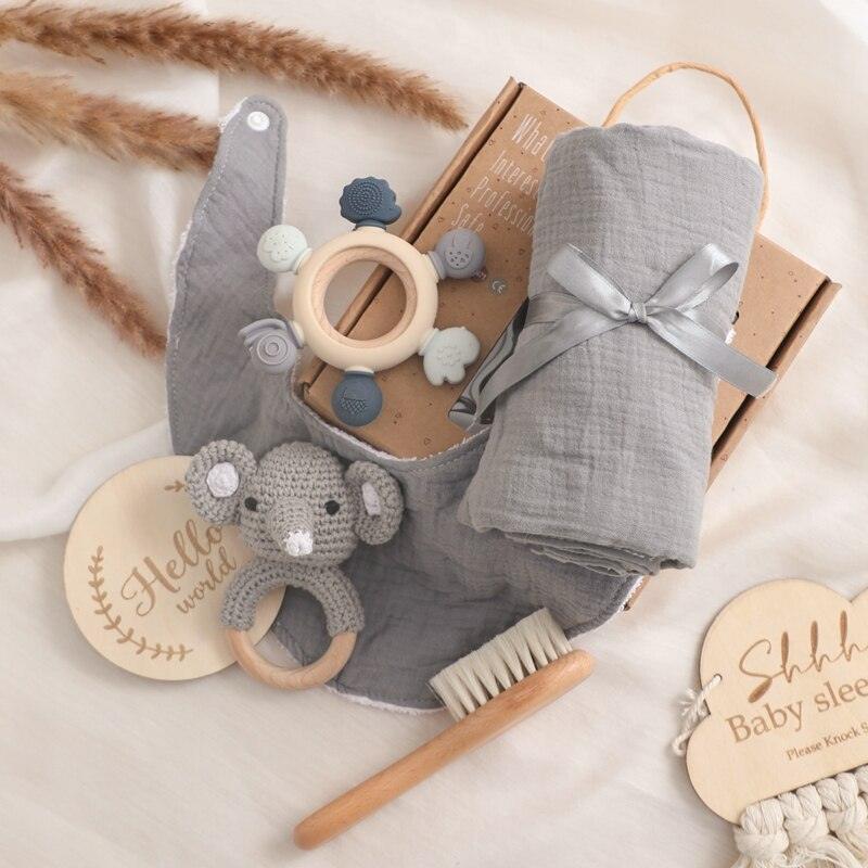 Das Liam Baby Geschenk zur Geburt von Hello World mit grauem Multifunktionstuch, Holzbürste, grauem Lätzchen, gehäkelter Koala-Rassel, Holz-Silikon-Beißring und Holzschildern - alles auf einer weichen Oberfläche angeordnet.