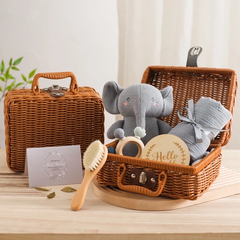 Das Matteo Baby Geschenk zur Geburt von Hello World besteht aus einem grauen Plüschelefanten, einer gerollten Decke, einer Babybürste aus Holz, einem Holz-Silikon-Beißring, einem Hello-Schild und einem Umschlag in einem Weidenkorb. Ein zweiter geschlossener Korb steht daneben.