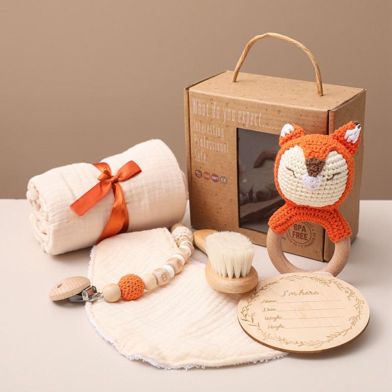 Das Hello World Rino Baby Geschenk zur Geburt Set enthält eine weiche Decke mit orangefarbenem Band, eine Schnullerklemme, eine Haarbürste aus Holz, einen Beißring für den Fuchs, ein Lätzchen und eine Holzkarte zur Geburtsanzeige - alles in einer braunen Schachtel.