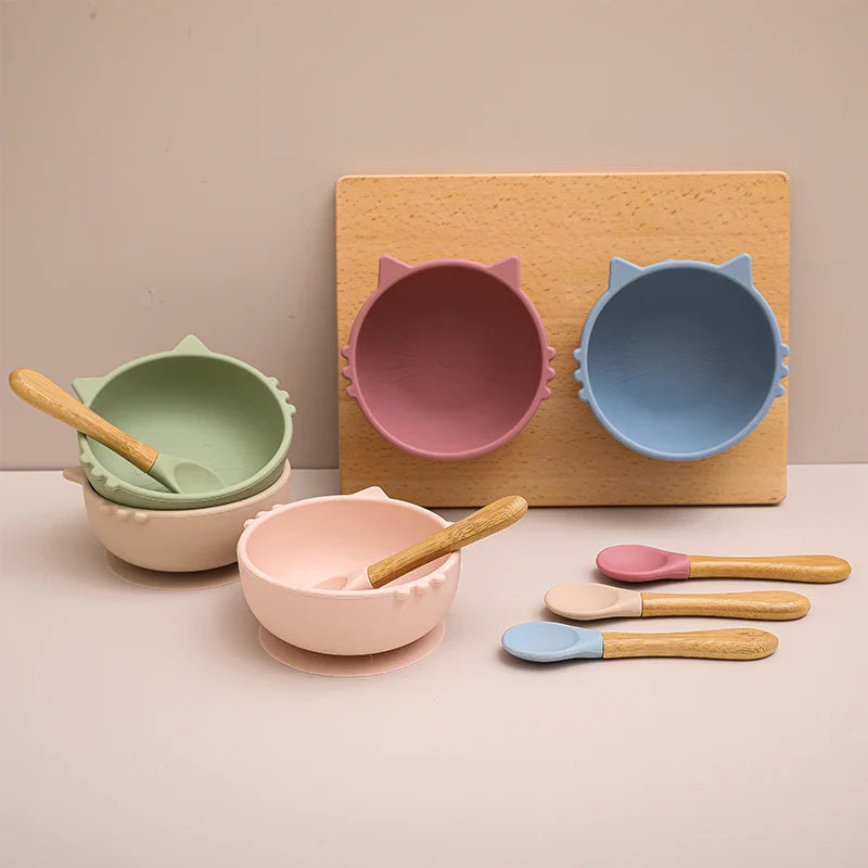 Four "Hello World" bowls round cat pink (12x5 cm), each with wooden handle silicone spoon; two stand upright, two are attached to the board with suction cups, and the four spoons are placed in front of them.