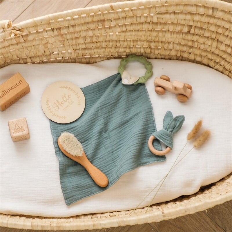Das Silas Baby Geschenk zur Geburt von Hello World besteht aus einem geflochtenen Körbchen mit grünem Stoff, einer Babybürste aus Holz, einem Holz-Greifling-Beißring, einem Spielzeugauto aus Holz, einer "Hello"-Karte, Holzklötzen und getrocknetem Weizen auf einer weißen Matratze.