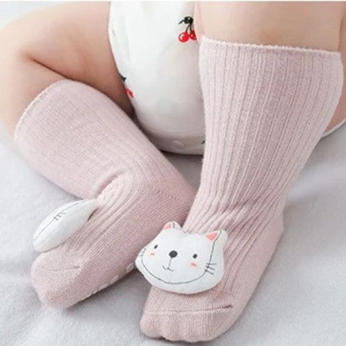 Ein Baby trägt die Socken Katze (Sohle: 6x11cm) von Hello World für 6-12 Monate mit Katzen-Design und sitzt auf weißem Untergrund. Der Strampler ist mit Kirschmuster verziert.