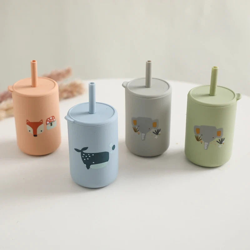 Quatre gobelets "Hello World" à motif bleu (6x12,5 cm), en silicone sans BPA, avec de jolis motifs de renard et de baleine et deux éléphants, aux douces couleurs pastel, joliment disposés les uns à côté des autres sur un fond clair.