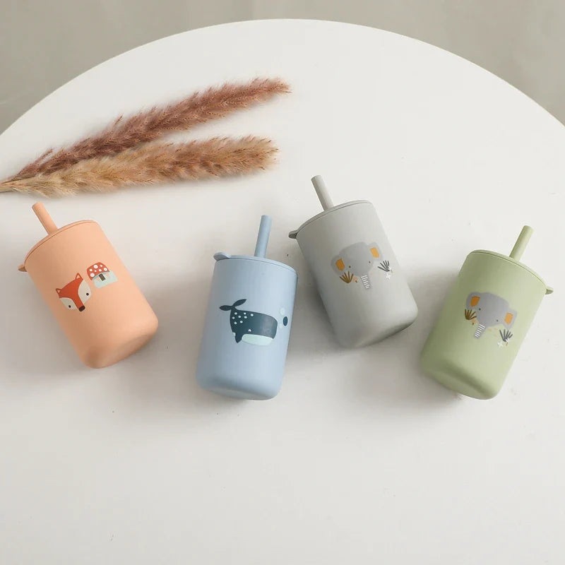 Quatre "gobelets à motif vert" sans BPA (6x12,5 cm) de Hello World avec des pailles et des motifs d'animaux - renard, baleine, éléphant et lion - se tiennent côte à côte sur un fond blanc à côté de deux pailles de séchage.