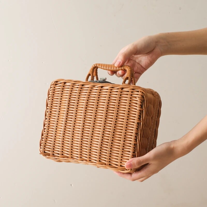 Eine Person hält das Xenia Baby Geschenk zur Geburt von Hello World in der Hand - eine rechteckige Handtasche aus Weidengeflecht mit geflochtenem Henkel - ein elegantes Accessoire zum Verschenken, dargestellt vor einem schlichten hellen Hintergrund.