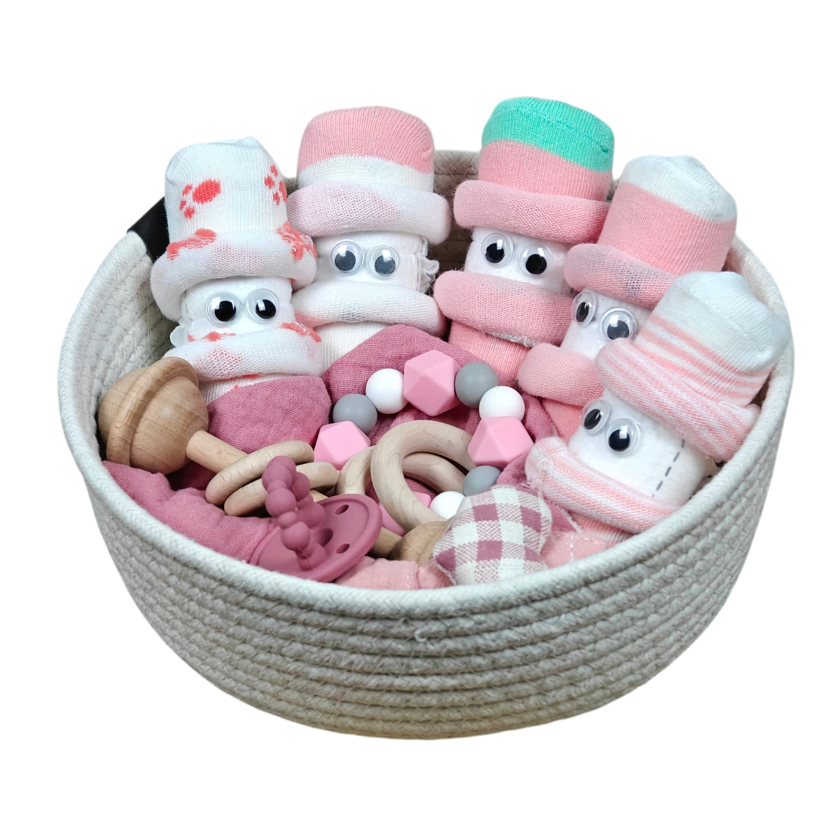 Das Kuschelkörbchen Blütenfünflinge von Hello World enthält Babygeschenke wie niedliche Socken mit Kulleraugen, Holz- und Silikonspielzeug sowie weiche rosa Tücher - gefertigt aus natürlichen Materialien.