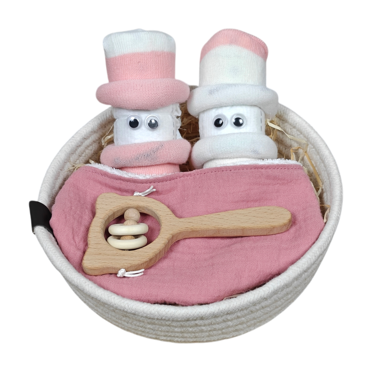 Ein weißes Körbchen enthält zwei puppenhaft gerollte weiße Handtücher mit rosafarbenen Mützen und Kulleraugen, ein rosafarbenes Tuch und eine hölzerne Babyrassel - ein bezauberndes Kuschelkörbchen-Blütenzwillinge-Babygeschenkset von Hello World.