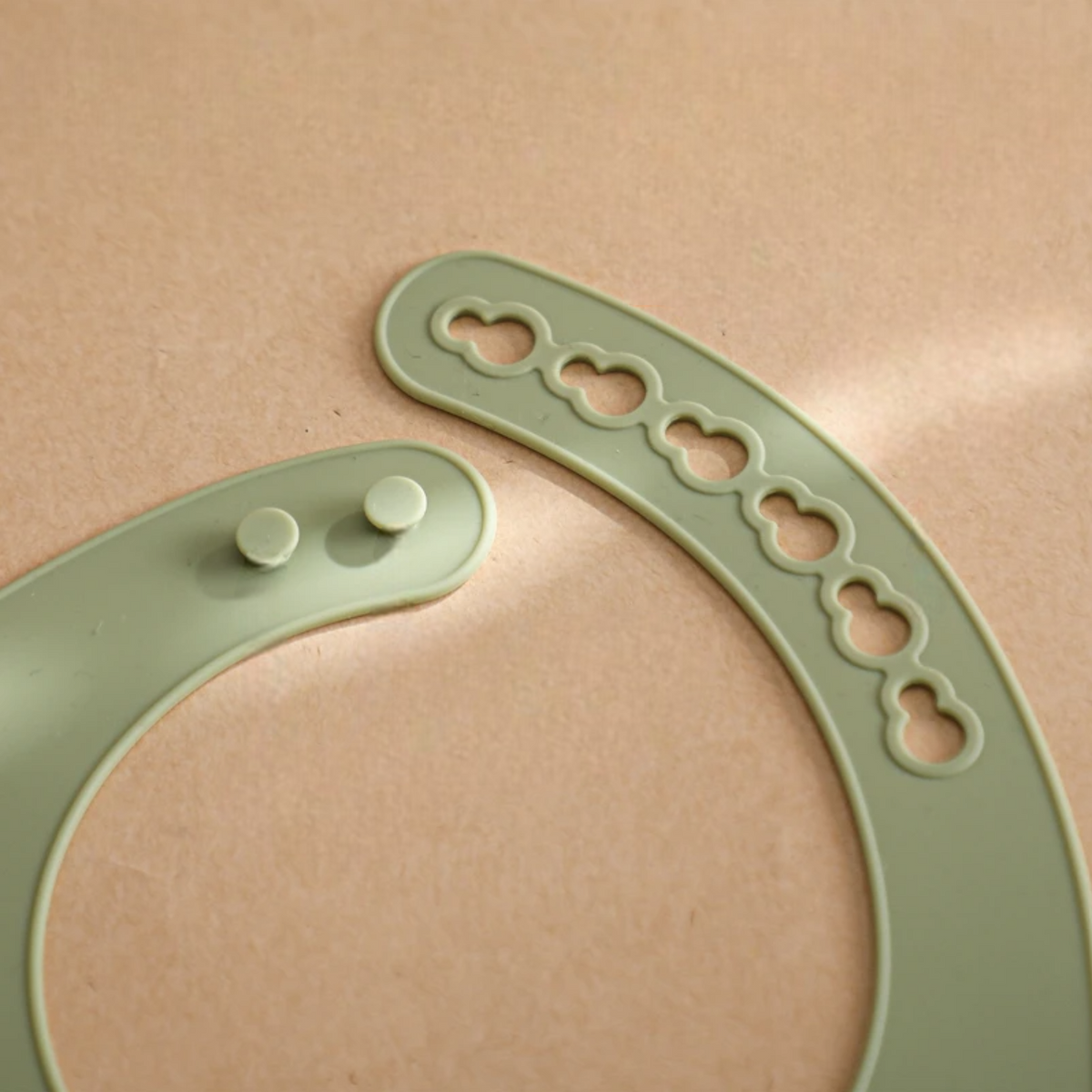 Nahaufnahme eines grauen Hello World Latzes mit Motiv aus Silikon (30x21cm), verstellbare Knopfverschlüsse, vor hellbraunem Hintergrund.