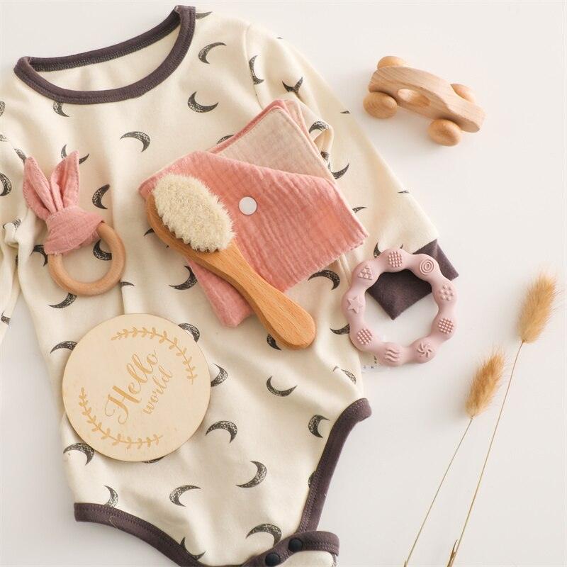 Das Lora Baby Geschenk zur Geburt von Hello World besteht aus einem cremefarbenen Strampler mit Halbmonden, einem Spielzeugauto aus Holz, Beißringen, einer weichen Bürste, Tüchern, einem "Hello World"-Schild aus Holz und getrockneten Gräsern - perfekt für die Begrüßung von Neugeborenen.
