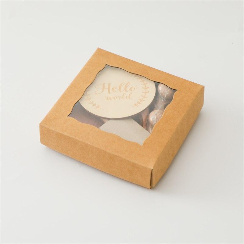 Das Lora Baby Geschenk zur Geburt von Hello World besteht aus einer braunen Geschenkbox mit Klarsichtfenster, in der ein runder "Hello World"-Keks, eingewickelte Süßigkeiten und ein süßer Holz-Greifling zu sehen sind - perfekt zum Verschenken.
