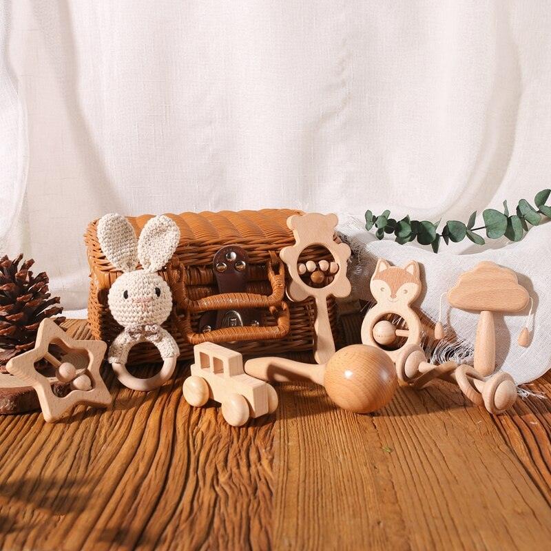 Das Maxin Baby Geschenk zur Geburt von Hello World umfasst nachhaltiges Holzspielzeug (Stern, Hase, Bär, Fuchs, Pilz, Auto, Holzrassel) - perfekt als Baby Geschenk - hübsch arrangiert vor einem Korb auf Holzboden mit weißen Vorhängen.