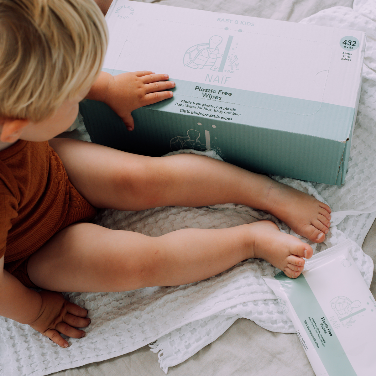 Toddler next to the Naïf large pack of 432 plastic-free baby wipes made from biodegradable eucalyptus fibers.