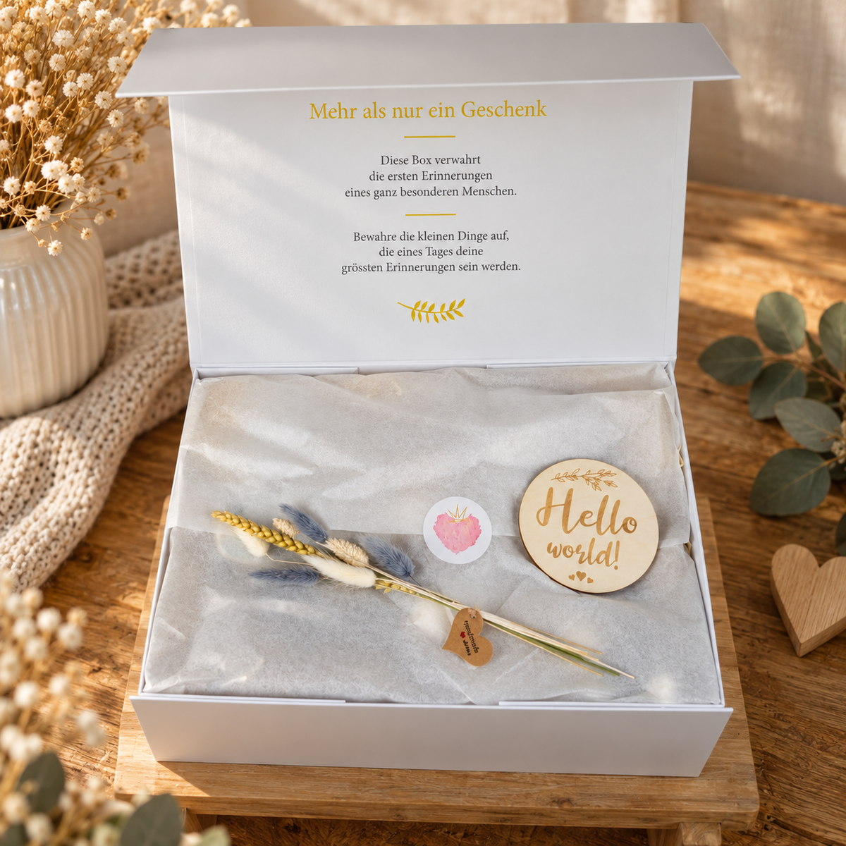 Geöffnete weisse Geschenkbox mit Seidenpapier, Trockenblumen, Hello World Holzschild und liebevollen Details als Erinnerungsbox zur Gebur