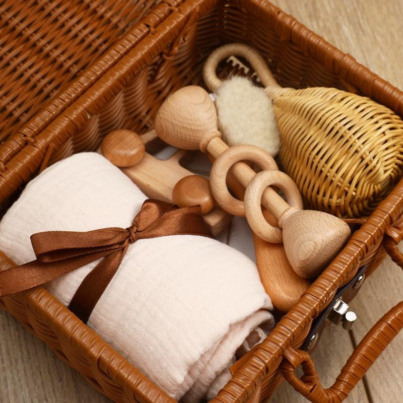 The Rusty Baby birth gift from Hello World consists of a woven basket with a rolled cream blanket, wooden toys, a soft brush, baby milestone cards and a small rattle - beautifully arranged on wood.