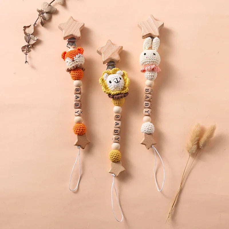 Drei Hello World Schnullerketten mit Aufschrift "Baby" Fuchs (30x4,5cm) Schnullerclips mit Tiermotiven und Holzstern-Clips sind auf einem beigen Hintergrund mit getrockneten Pflanzen abgebildet - charmant und sicherheitsgeprüft.