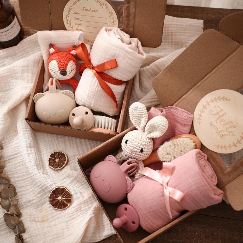 Das Serena Baby Geschenk zur Geburt von Hello World enthält zwei offene Geschenkboxen mit Kuscheldecken, einem Rasselhase, Silikonrasseln, einem Schnuller-Set und weiteren Utensilien - hübsch arrangiert und ideal als Babygeschenk.