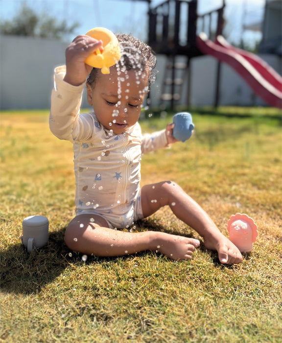 Child plays with the Small Foot silicone bath toy set in the garden and splashes water.