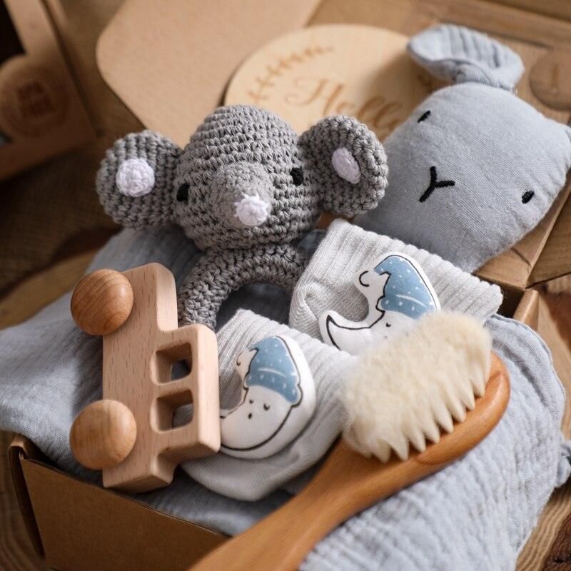 Das Snuh Baby Geschenk zur Geburt von Hello World: Liebevoll arrangierte Box mit grauem Stoffhasen, Schnuffeltuch Elefant, Holzauto, Babybürste und Söckchen mit Mond- & Sternmotiv auf weichem, grauem Stoff.