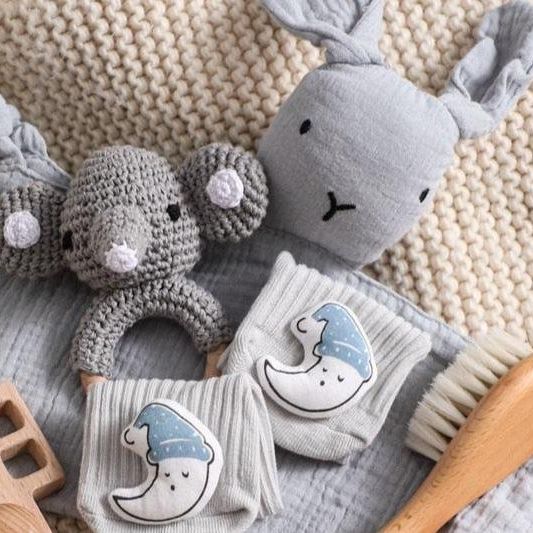 Snuh Baby Geschenk zur Geburt von Hello World: mit gehäkelter grauer Tierrassel, Schnuffeltuch Elefant, Mondsocken, blauer Mütze, Beißring aus Holz, Bürste und cremefarbener Decke - das perfekte nachhaltige Babygeschenk.