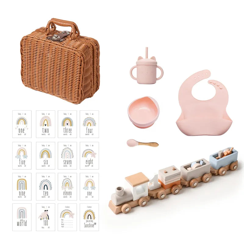 Das Hello World Tiffany Baby Geschenk zur Geburt besteht aus einem Weidenkorb, einer rosafarbenen Schnabeltasse, einer Schüssel, einem Löffel, einem Silikonlätzchen, einer nostalgischen Holz-Lokomotive und Regenbogenkarten mit den Nummern eins bis zwölf.