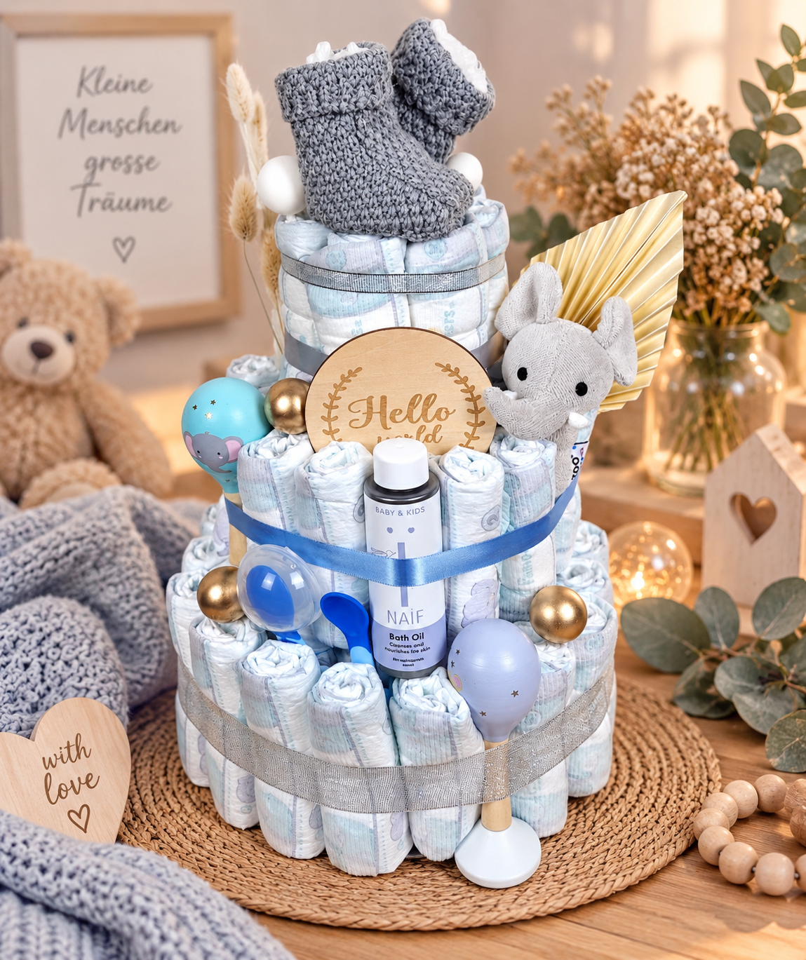 Torta di pannolini realizzata con amore in blu, grigio e argento con coccole, olio da bagno NAÏF, scarpine per bambini lavorate a maglia, elefante, sonagli per bambini e cartello in legno come regalo di nascita.