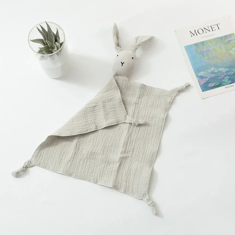 Eine weiche, hellgraue Hasendecke liegt auf einer weißen Fläche neben einer kleinen Pflanze in einem Glastopf und einem Kunstbuch mit dem Titel Monet, das auf dem Einband ein Seerosenbild zeigt.