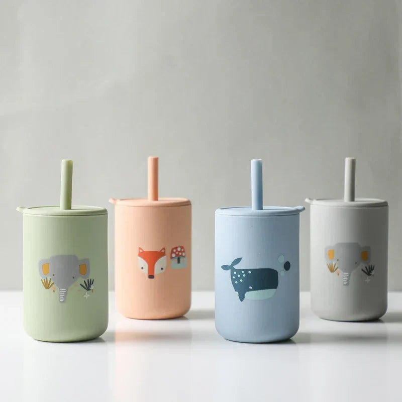 Vier pastellfarbene Becher mit Deckel und Strohhalm, jeder mit einer anderen niedlichen Tierillustration: Elefant, Fuchs, Wal und einem minimalen Design, vor einem schlichten Hintergrund.