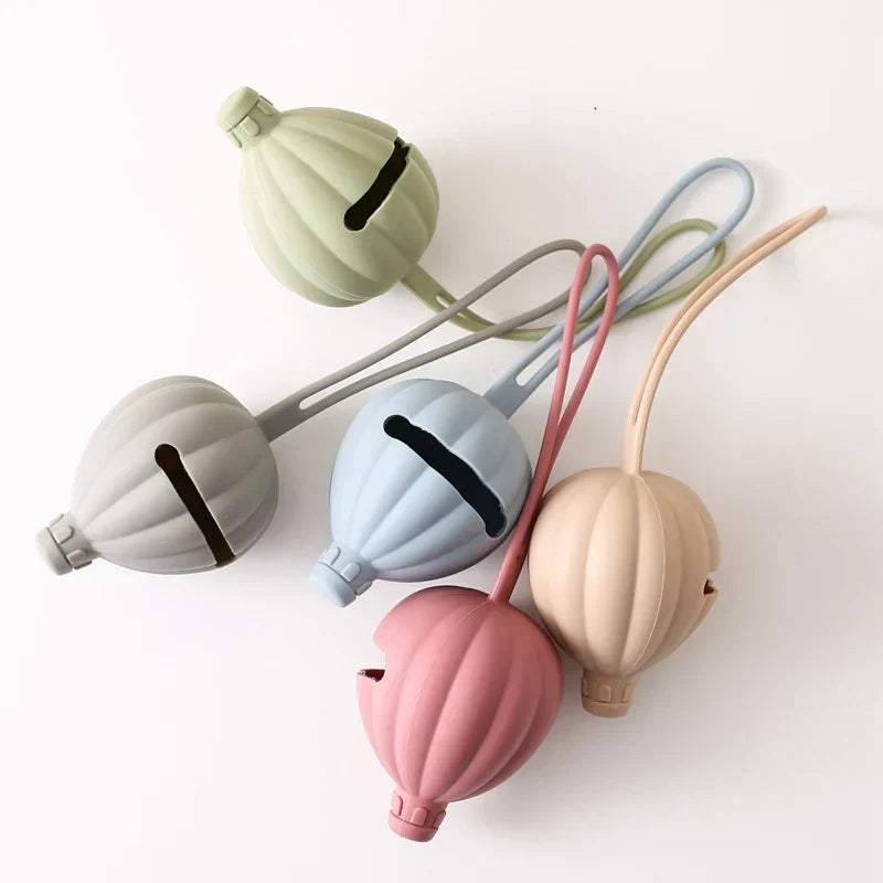 Fünf ballonförmige Silikonbeutelverschlüsse in Pastellfarben - grün, blau, grau, rosa und beige - sind auf einer weißen Fläche angeordnet. Jeder hat einen Schlitz und einen Griff mit Schlaufe.