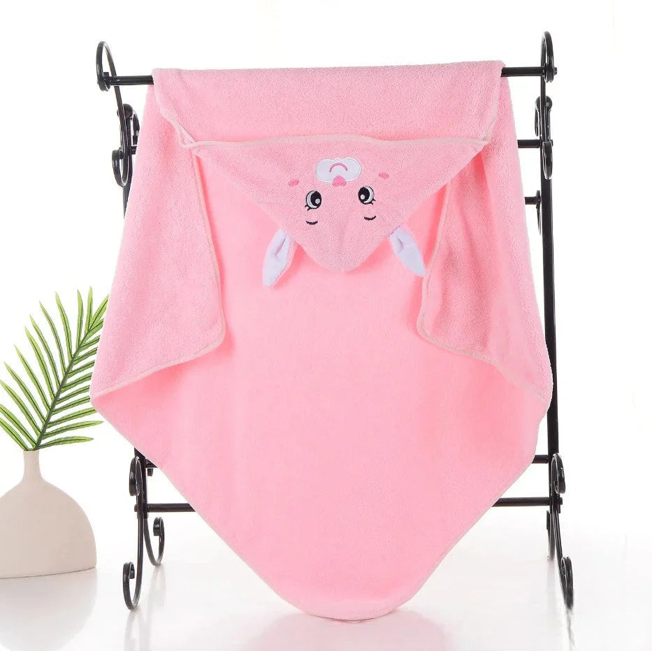 Ein rosafarbenes Babyhandtuch mit Kapuze mit einem niedlichen Tiergesicht und Ohren auf der Kapuze, drapiert über einem schwarzen Metallhandtuchhalter. In der Nähe steht eine kleine Pflanze in einer weißen Vase.