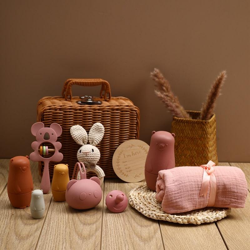 Das Ayla Baby Geschenk zur Geburt von Hello World besteht aus Tierfiguren, einem Koala-Greifling, einem gehäkelten Häschen, einem Silikon-Schnuller und einer Holzrassel - wunderschön arrangiert auf einer gewebten Matte mit Pampasgras in einer Vase.