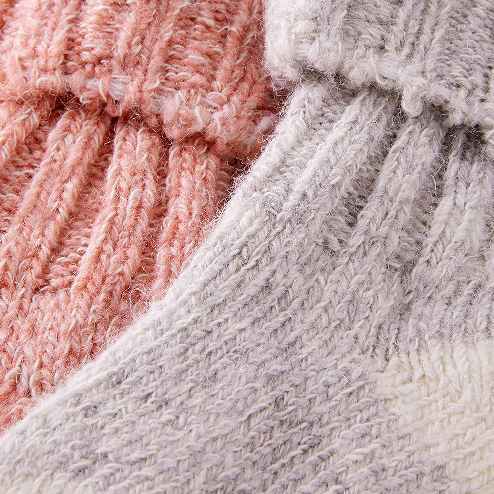 Detailaufnahme der gestrickten Babysocken mit Wolle in Rosa und Hellgrau