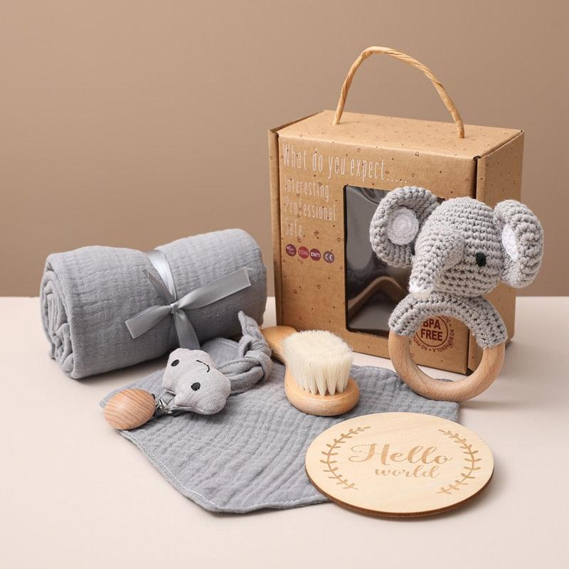 The Fabio Baby gift for the birth of Hello World consists of a gray blanket, a crocheted elephant rattle, a soft brush, a wooden "Hello World" sign, a pacifier clip and a gray cloth - nicely arranged in front of a handy brown box.