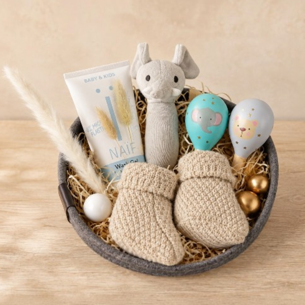 Baby Geschenkkorb gefüllt mit Fiechtenholzwolle und Markenprodukten, Dekoriert mit ziergrass und goldene und weisse Dekokugeln.