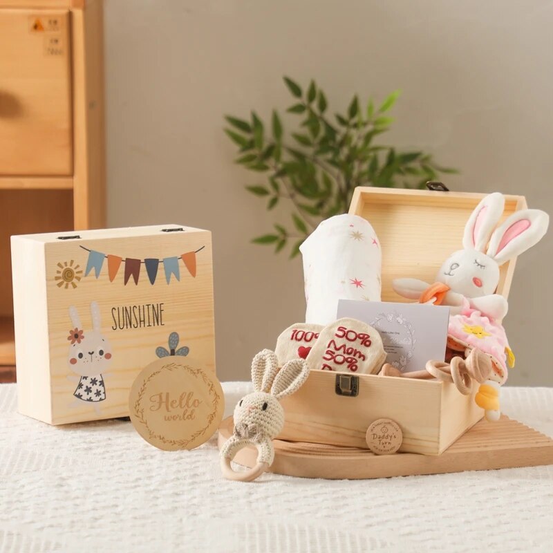 Das Anna Baby Geschenk zur Geburt von Hello World ist eine Geschenkbox aus Holz mit der Gravur Sonnenschein", gefüllt mit einem Rasselhasen aus Plüsch, einem Kuscheltier, einem Lätzchen, einer Karte, einem Beißring und einer Plakette mit dem Schriftzug Hallo Welt" - perfekt für die Begrüßung eines neuen Babys.