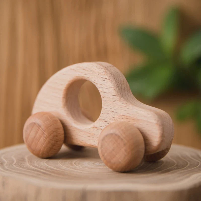 Das kleine, runde Holzauto "Auto Rund aus Holz [8.5x4cm]" von Hello World steht auf einer hellen Holzoberfläche, im Hintergrund ist eine grüne Pflanze zu sehen - nachhaltiges Spielzeug für umweltbewusste Familien.