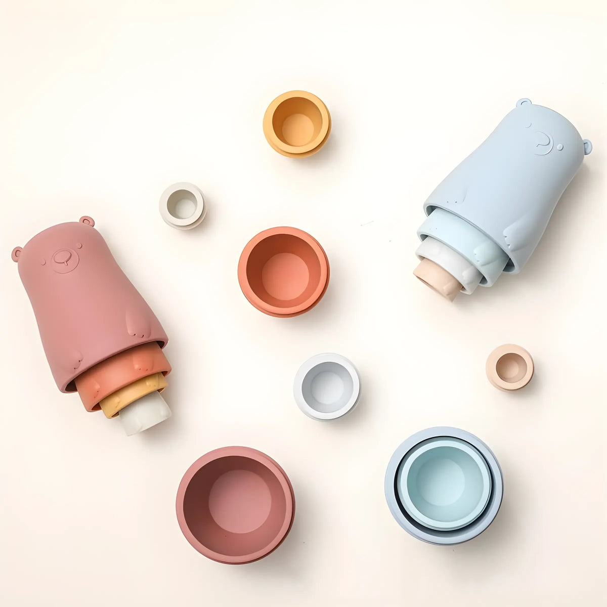 Zwei Sets von Hello World Bär Rot aus Silikon [6x13cm], eines in Rosa und eines in Blau, werden auf einer hellen Fläche ausgestellt. Die farbenfrohen Nistkästen sind getrennt und in verschiedenen Größen um sie herum gestapelt, um spielerisch zu lernen.