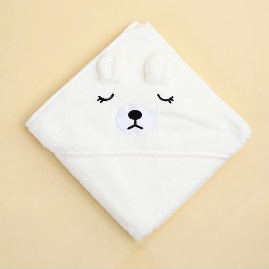 Das Hello World Badetuch mit Kapuze Eisbär [80x80cm] in Weiß, quadratisch gefaltet, zeigt ein süßes Bärengesicht mit geschlossenen Augen, schwarzer Nase und 3D-Ohren - das ideale Geschenk zur Geburt auf beigem Hintergrund.