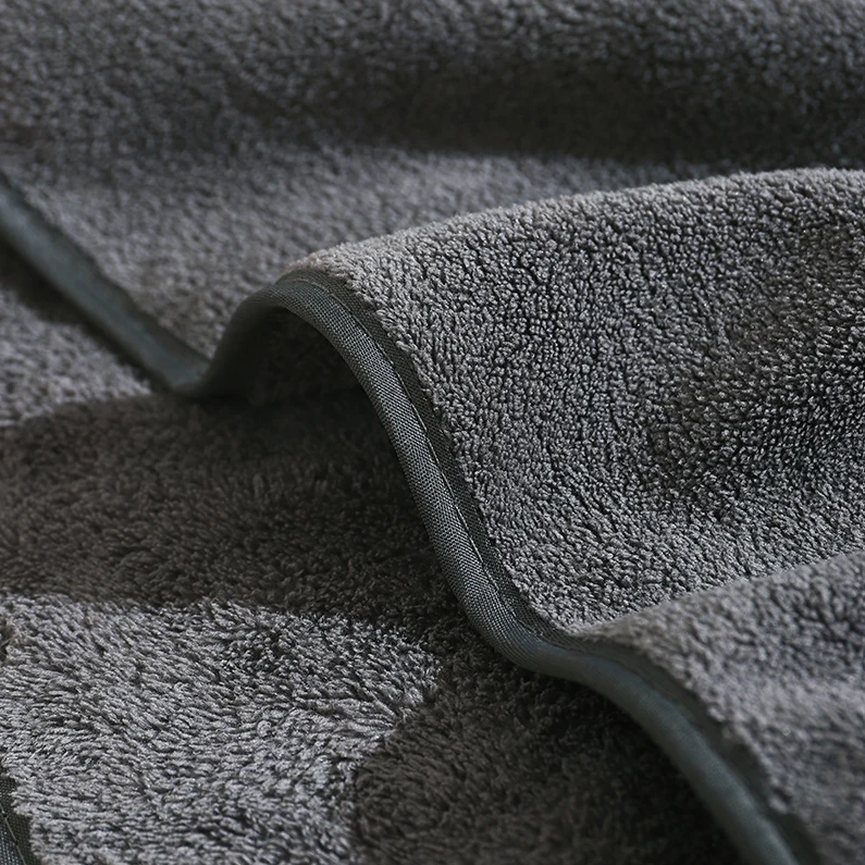 Eine Nahaufnahme des Hello World Badetuchs mit Kapuze Elefant [80x80cm] zeigt den weichen, dunkelgrauen Frotteestoff mit plüschiger Textur und sauber verarbeiteten Kanten, die sanfte Falten und Schatten hervorheben.