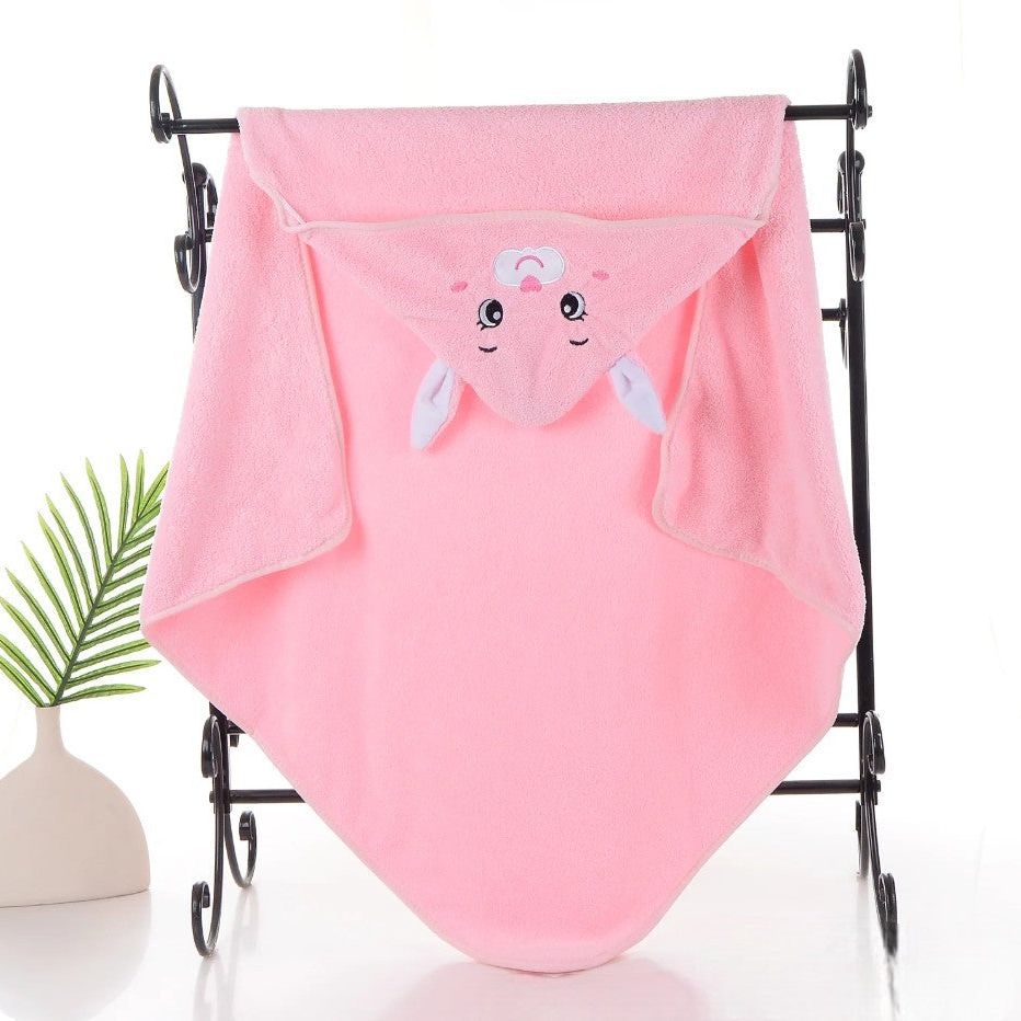 Ein rosafarbenes Hello World Badetuch mit Kapuze Hase (80x80cm) mit einem niedlichen Tiergesicht und Ohren hängt an einem schwarzen Metallgestell, neben einer kleinen grünen Pflanze in einer weißen Vase auf einer weißen Fläche.