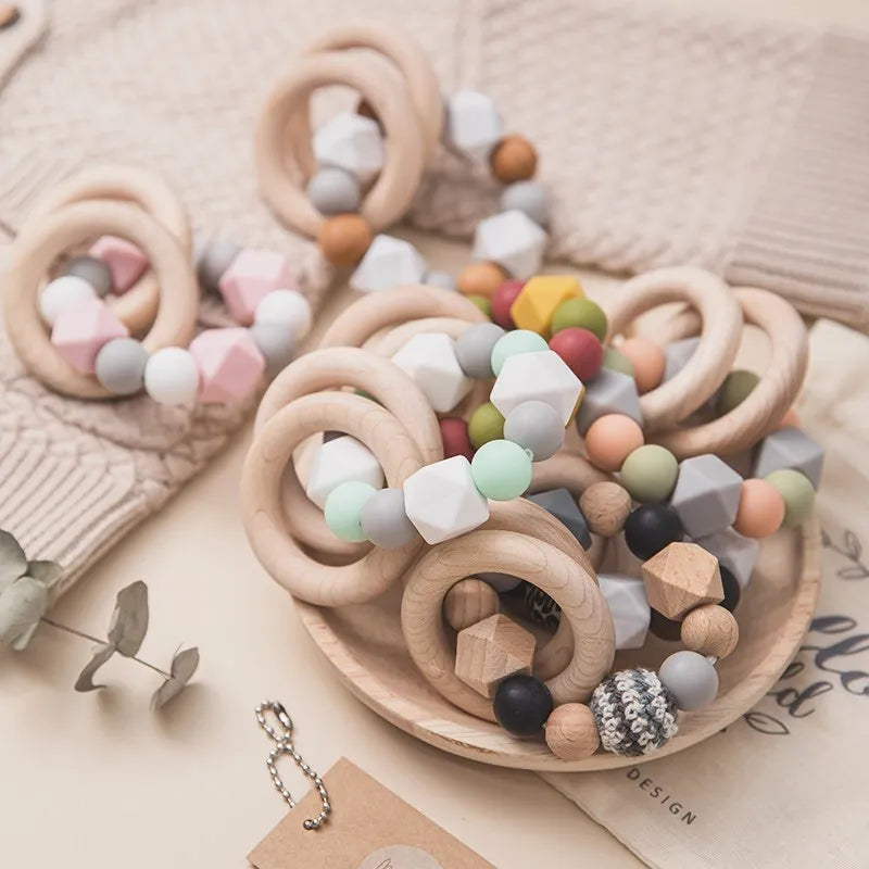 Die Hello World Beissring Kette Duo Gelb [7x9cm] besteht aus bunten Silikonperlen, geometrischen Formen und Ringen, die auf einem Teller und einer beigen Oberfläche für einen verspielten, gemütlichen Look sorgen.