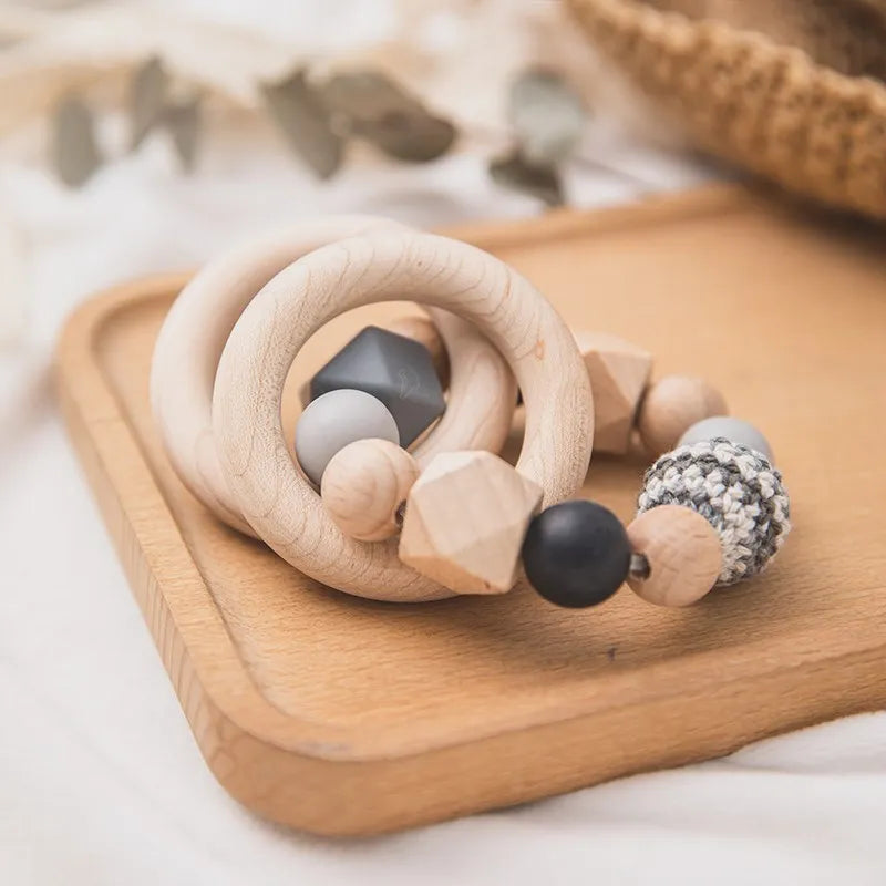 Die Beissring Kette Duo Schwarz [7x9cm] von Hello World besteht aus Holz-, Häkel- und Silikonperlen in Natur-, Schwarz- und Grautönen mit Ringen, die auf einem Holztablett präsentiert werden.