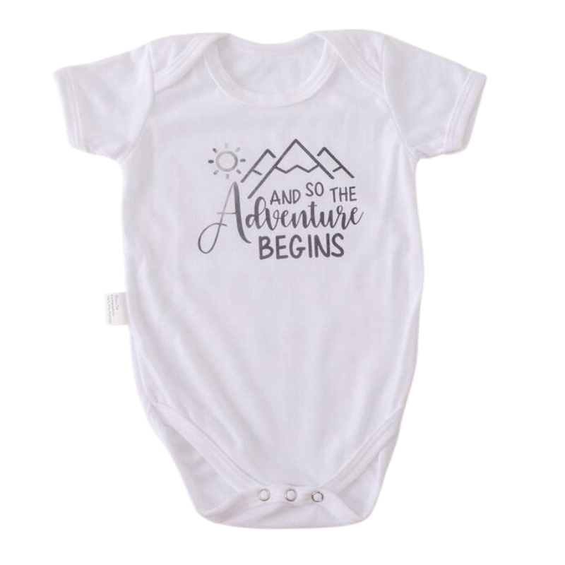 Der Hello World Body [33,5x38cm] (6-9 Monate) in Weiß hat kurze Ärmel, einen Sonnen- und Bergaufdruck sowie "And so the adventure begins" in Schwarz auf der Vorderseite. Hergestellt aus weicher Baumwolle für extra Komfort.